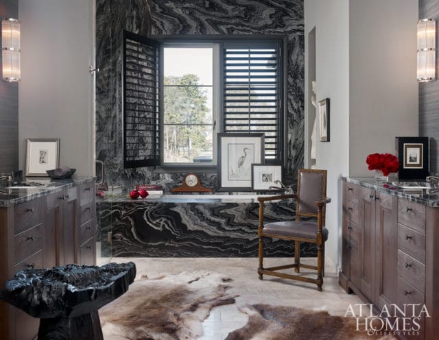 Luxurious bathroom with dark wood vanities, marble countertops, a black and white marble bathtub surround, and animal hide rugs on the floor.
