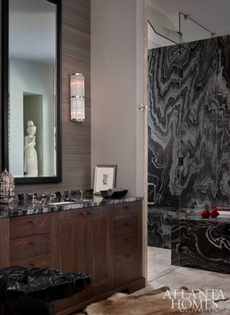 Dark wood vanity with marble countertop and backsplash, flanked by a large mirror and a glass-enclosed shower with dramatic black and white marble walls.