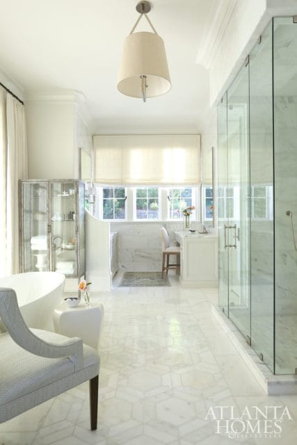 White marble bathroom with freestanding tub, glass shower, vanity, and geometric marble floor. A decorative pendant light hangs from the ceiling.