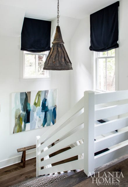 Staircase landing with white railings, abstract art, a rustic wooden bench, and a large metal pendant light