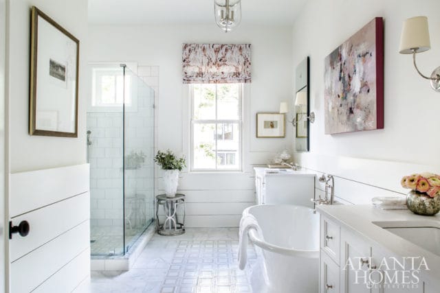 White bathroom with a freestanding tub, glass-enclosed shower with white subway tile, double vanity, and abstract art above the vanity.