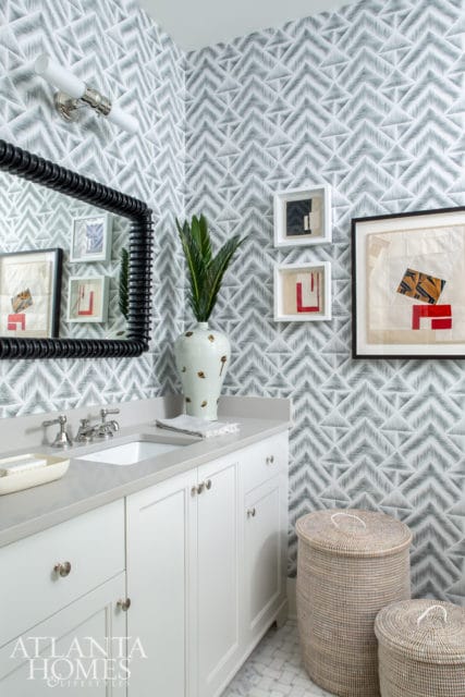 Powder room with gray and white geometric wallpaper, white vanity with quartz countertop, chrome fixtures, and a large black framed mirror.