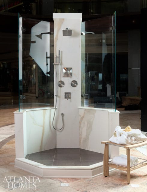 Corner shower with glass enclosure, marble accent walls, and brushed nickel fixtures. A wooden bench with towels sits to the right.
