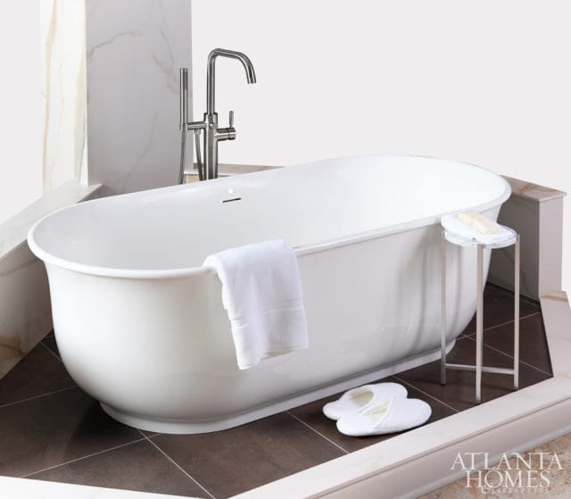 White freestanding bathtub with chrome floor-mounted faucet, white towels, slippers, and marble accents.
