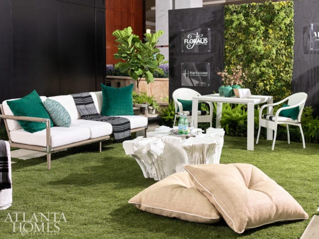 Outdoor living space with white sectional sofa, green accent pillows, striped throw blanket, and a white abstract coffee table on artificial grass.