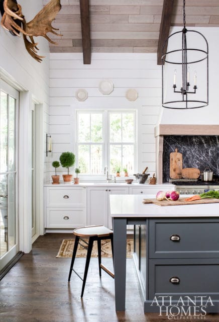 White shiplap kitchen with dark gray island, marble backsplash, wood ceiling beams, and a large black lantern chandelier.