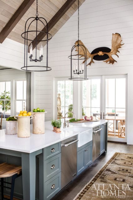 Farmhouse kitchen with white shiplap walls, vaulted wood-beamed ceiling, and a large island with a white farmhouse sink and grey cabinetry.