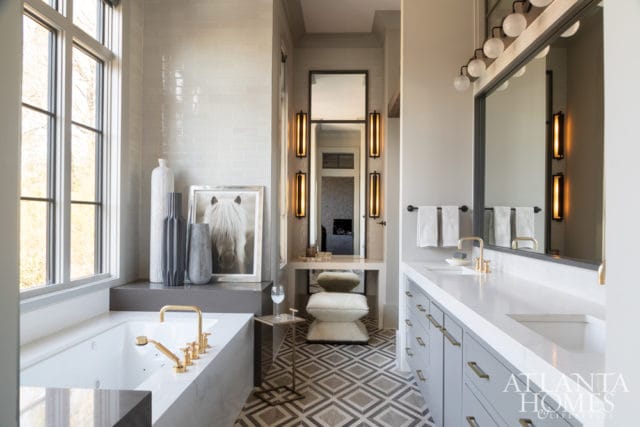 Luxury bathroom with a white soaking tub, gold fixtures, a double vanity with gray cabinetry and white countertops, and a geometric patterned floor.