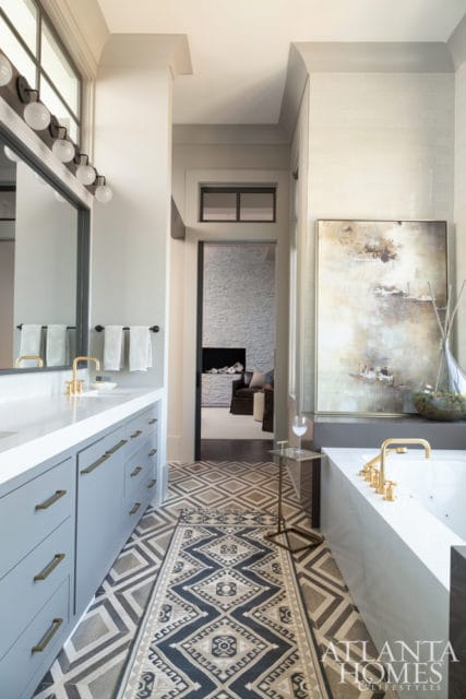 Light blue vanity with brass hardware, white countertop, and large mirror in a bathroom with geometric floor tile and a freestanding tub.