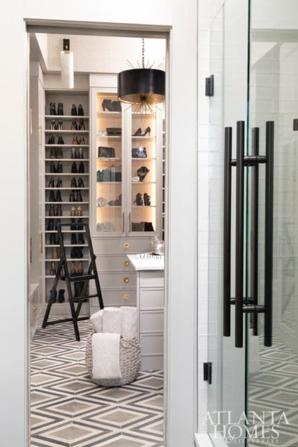 Walk-in closet with gray cabinetry, open shelving displaying shoes and handbags, glass-fronted cabinets, a black starburst chandelier, and a geometric tile floor.