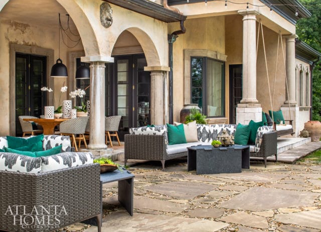 Covered patio with stone flooring, wicker furniture with patterned cushions, and a hanging swing chair.