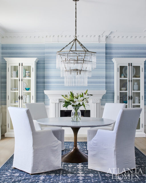 In the dining room, a three-tiered bronze-and-glass chandelier illuminates a metal-and-dulled brass dining table with a Carrera marble top from RH Modern. The rug is from Moattar, Ltd.
