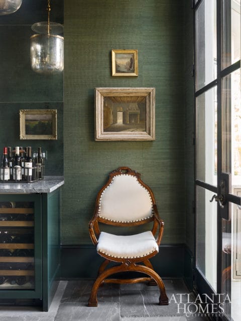 Green grasscloth wallpapered room with a vintage wooden chair upholstered in white fabric, a wine fridge, and framed artwork on the wall.
