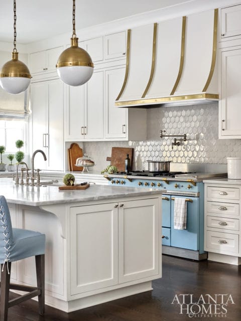 White kitchen with marble island, blue range, brass accents on range hood, and globe pendant lights.