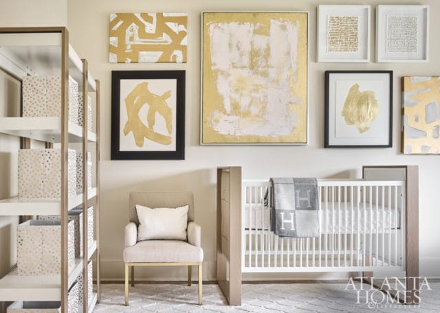 Nursery with a white crib, a beige armchair with a white pillow, gold and white abstract art on the wall, and white shelves filled with gold-dotted storage bins.