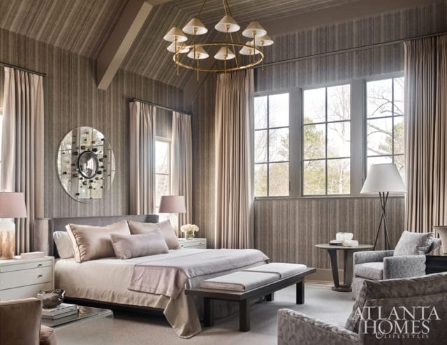Bedroom with striped wallpaper, a king-sized bed with neutral linens, a circular wine rack on the wall, and large windows overlooking trees.