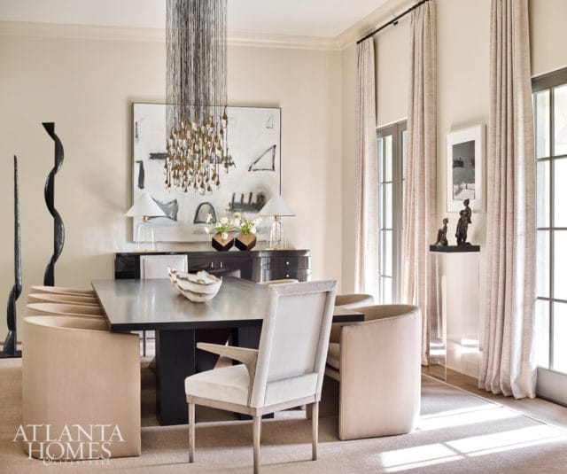 Dining room with a dark wood table, upholstered chairs in neutral tones, a large abstract painting, and a dramatic beaded chandelier.