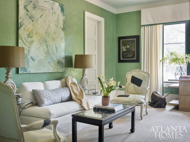Living room with green textured walls, white sofa with patterned pillows, glass-top coffee table, and ornate armchair.