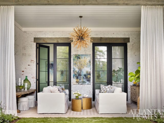 Covered porch with white brick walls, white slipcovered sofas, gold side tables, and a sputnik chandelier.