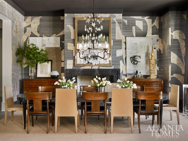 Dining room with a dark wood table surrounded by upholstered and wood chairs, a fireplace with a crystal chandelier above, and abstract wallpaper.