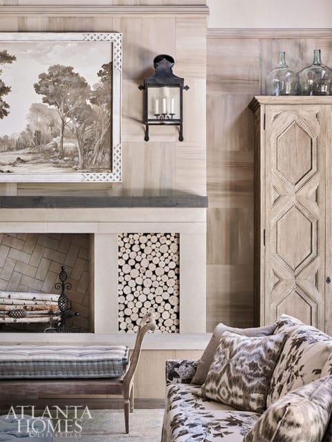 Living room with fireplace featuring a landscape painting, wood-paneled walls, a decorative cabinet, and patterned upholstery on seating.
