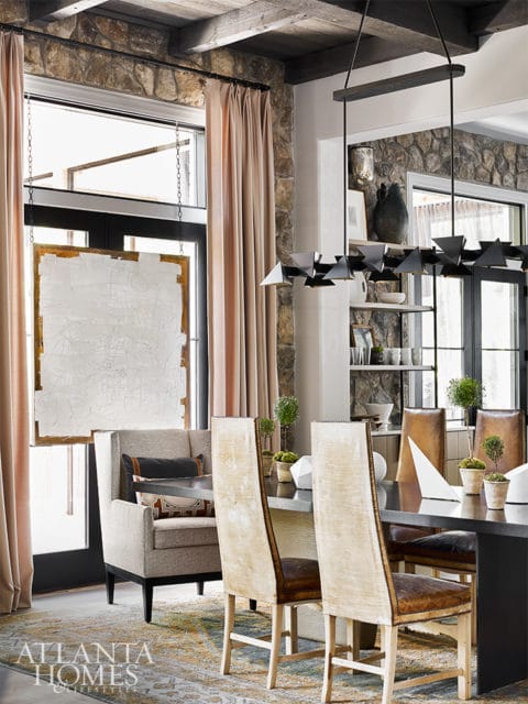 Dining room with stone accent wall, exposed wooden beams, neutral upholstered chairs, and a modern black chandelier.