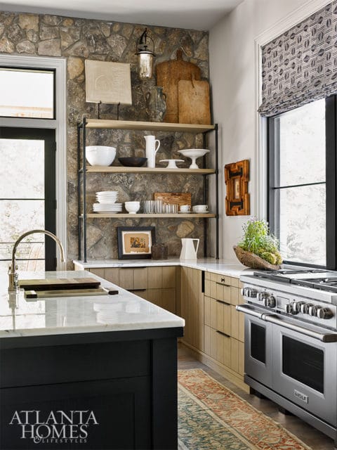 Kitchen with a stone accent wall, open shelving displaying white dishes and decor, a marble island, wood cabinetry, and a stainless steel range.