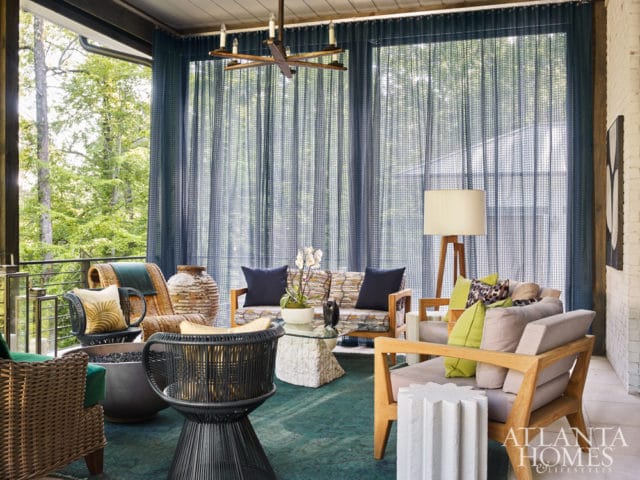 Covered porch with wicker and wood furniture, blue sheer curtains, and a chandelier.
