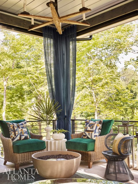 Covered porch with two wicker armchairs and green cushions, a large concrete fire pit, and a dark blue mesh curtain.