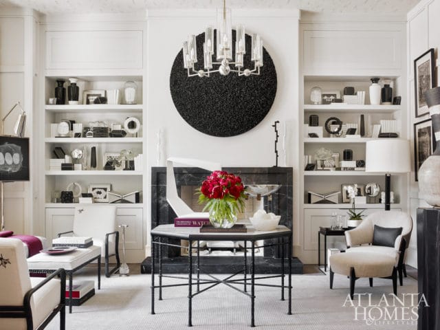 Living room with white built-in bookshelves flanking a black marble fireplace, a black circular textured wall art, and a glass chandelier.