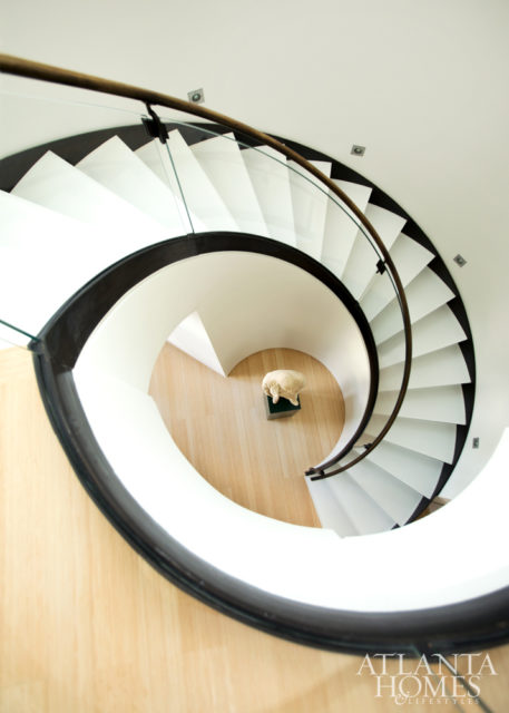 A spiral staircase with a glass railing leads to the second-floor bedrooms in the airy penthouse.