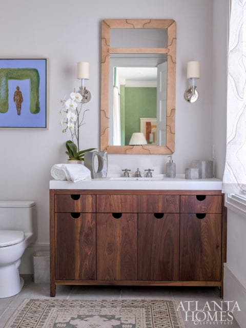 Bathroom with a dark wood vanity, white countertop, modern faucet, and a framed mirror with a tan leather border. A white toilet and a patterned rug are visible.