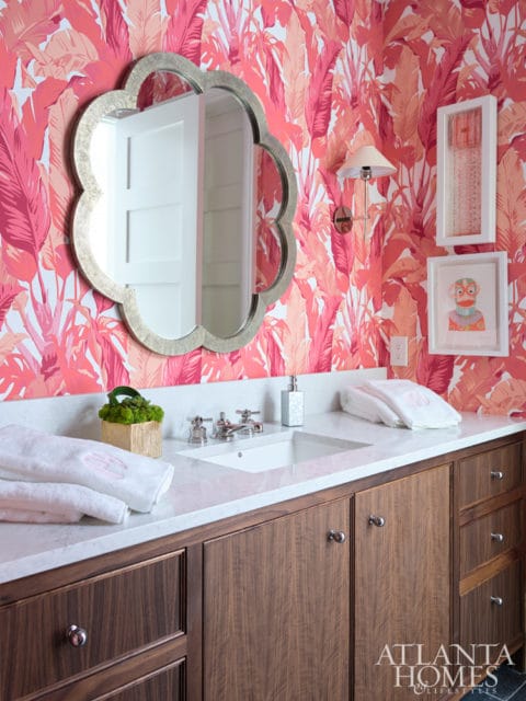Bathroom vanity with dark wood cabinets, white quartz countertop, and a floral wallpaper in shades of pink and coral. A scalloped mirror hangs above the sink.
