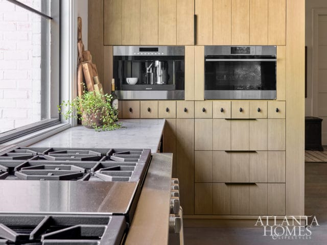 Modern kitchen with light wood cabinetry, built-in coffee maker and oven, marble countertops, and a professional gas range.
