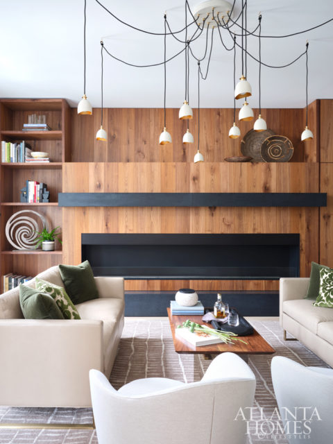 A bespoke walnut fireplace by Skylar Morgan Furniture is showstopping in the den. The Hinkley Lighting fixture nods to the home’s art-centric ambience. The wool-and-silk rug is custom by Verde Home.