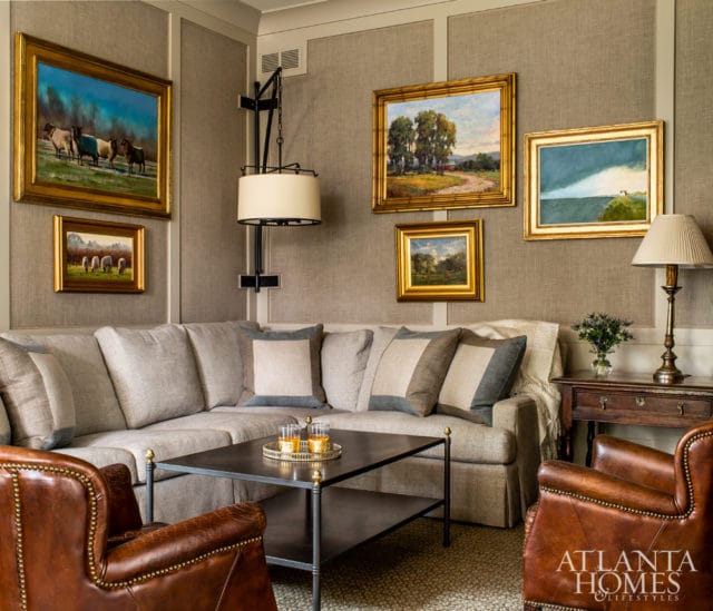 Living room with a sectional sofa, two leather armchairs, a dark metal coffee table, and framed landscape paintings on a textured wall.