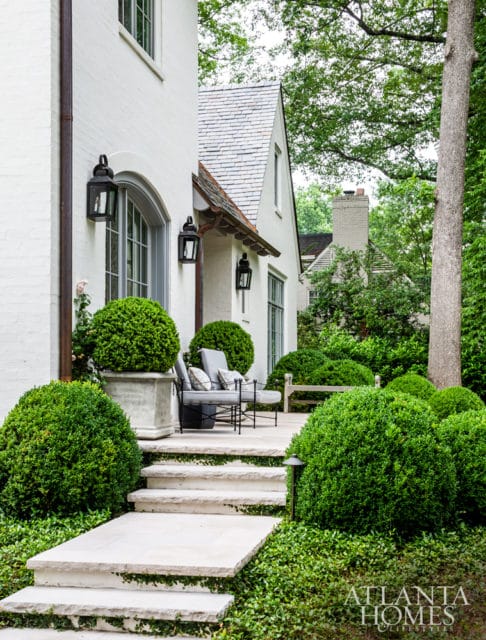 White brick house with slate roof, arched windows, black lanterns, stone steps, and manicured boxwood bushes.