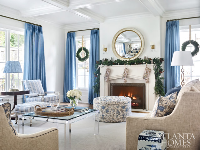 Blue linen draperies by Fabricut enliven the white walls in the living area, where a sofa and love seat from Wesley Hall surround a custom limestone mantel from Materials Marketing. The bespoke fireplace screen is Lucy Smith from Holland MacRae.