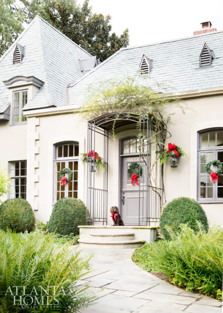 The façade shows off its French leanings with stucco walls and a slate roof. Sporting a shiny red ribbon, pup Rosie greets guests during the holidays.
