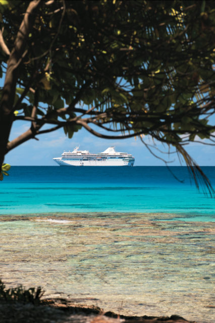 A Paul Gauguin ship is visible through lush tropical foliage of Rangiroa, French Polynesia.