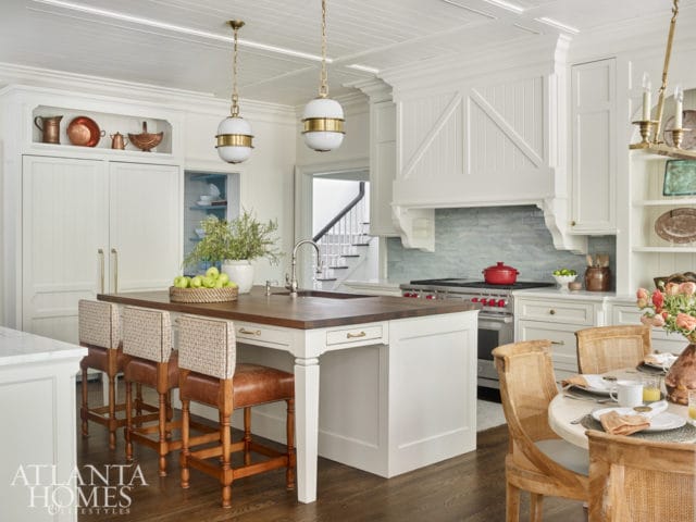 White kitchen with a large island topped with a butcher block, paneled cabinetry, a light blue subway tile backsplash, and brass accents.