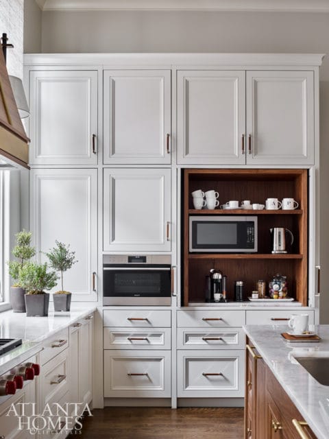 White kitchen with built-in coffee station featuring a microwave, coffee maker, and mugs on wooden shelves, flanked by white cabinetry and a Wolf oven.
