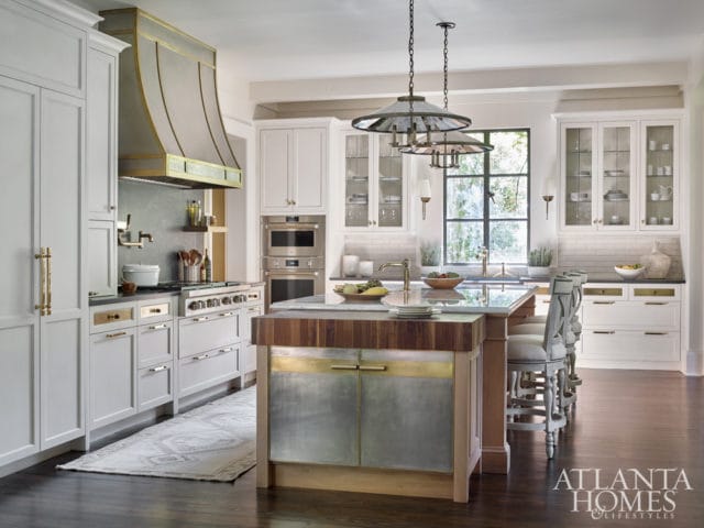 Light gray kitchen with a large metal range hood, white cabinetry, a marble island with a butcher block top, and dark wood floors.
