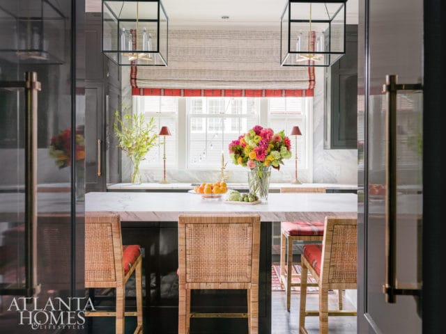 Dark gray kitchen with white marble countertops, rattan bar stools with red cushions, and a large floral arrangement on the island.