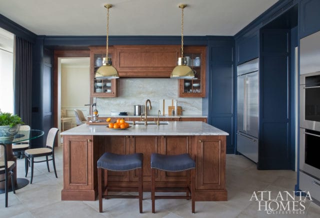 Kitchen with navy blue cabinetry, a large wooden island with marble countertop, brass pendant lights, and stainless steel appliances.