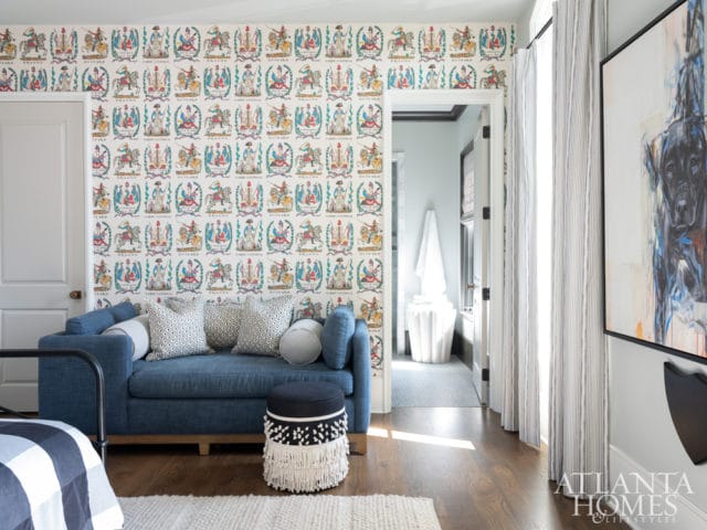 Blue sofa with patterned pillows in a room with whimsical wallpaper and a large abstract dog painting on the wall.