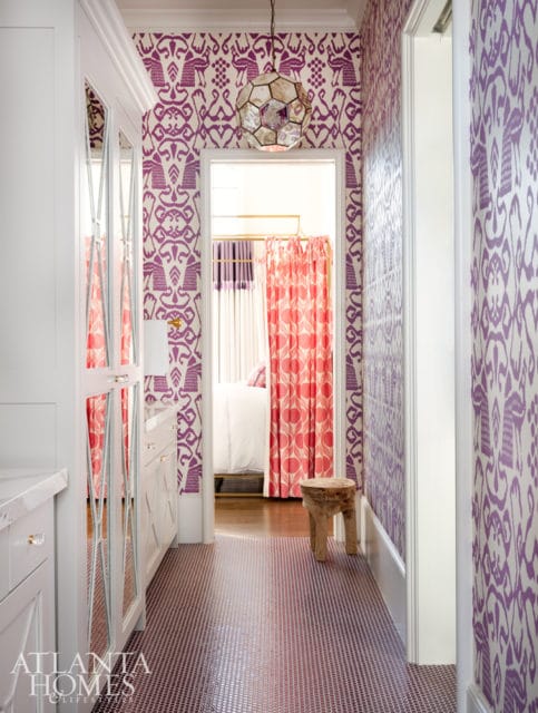 Hallway with purple and white patterned wallpaper, a geometric pendant light, and a doorway revealing a bedroom with coral curtains and a white bed.