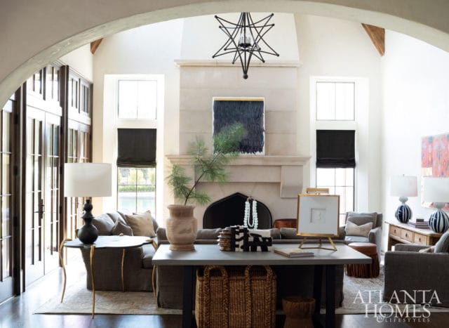 Living room with a large stone fireplace, arched doorway with glass doors, and plush seating. A starburst chandelier hangs above the fireplace.