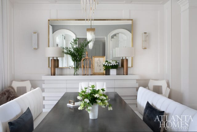 Modern dining room with a dark wood table, white upholstered banquette seating, a white buffet with stacked drawers, and a large gold-framed mirror above.