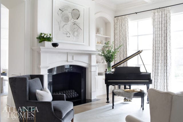 Living room with a white fireplace, abstract art, a black grand piano, and gray upholstered chairs.